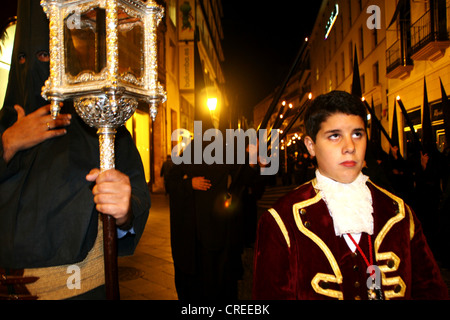Procession of a fraternity, Cofradia, during the Holy Week, on the night with black hoods and boy in medieval garb and looking with disbelief, Spain, Andalusia, Sevilla Stock Photo