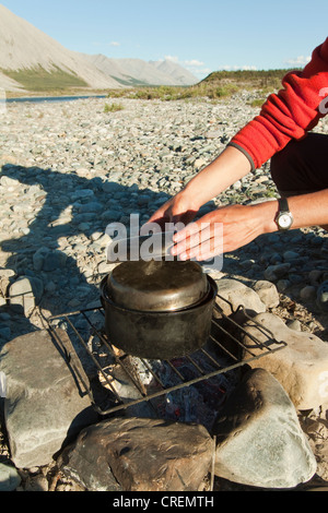 Backing bread on a camp fire, covering the large pot with a lid, inside there are pebbles, water and a covered small pot, then Stock Photo