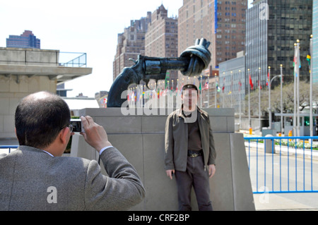 tourists taking souvenir photos in front of the knotted gun, non-violence sculpture from Reuterswaerd in front of UN Headquarter, USA, USA, New York City, Manhattan Stock Photo