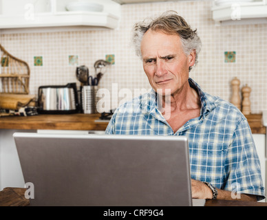Older man using laptop in kitchen Stock Photo