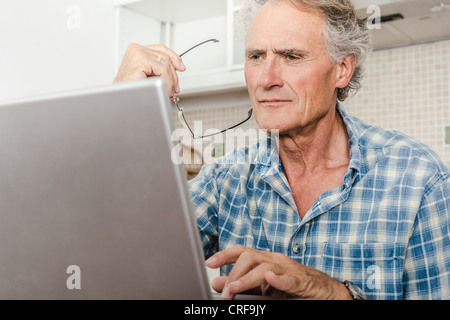 Older man using laptop in kitchen Stock Photo