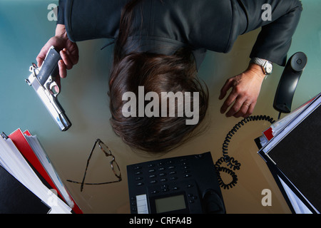 Businessman with gun face down on desk Stock Photo