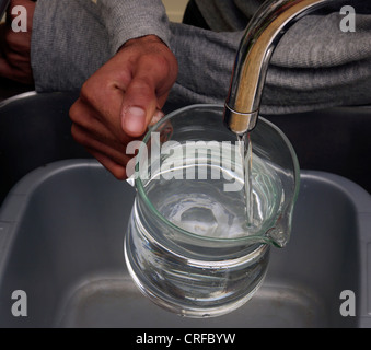 Afro-Caribbean Man's Hands Filling Water In A Glass Jug From A Tap Stock Photo