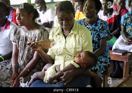 Mother fans out cool air to her sleeping baby in a church on Bougainville Island, Papua New Guinea