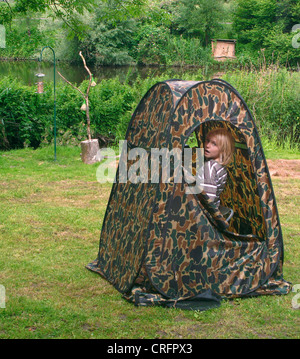 child sitting in camouflage tent watching birds, Germany Stock Photo