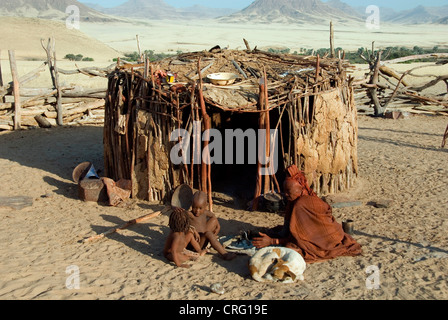 traditional Village of Purros, Himba woman with children and dog in front of a hut, Namibia, Purros Stock Photo