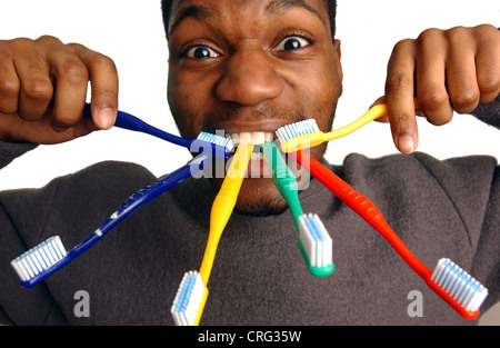 A conceptual image of a young man holding four toothbrushes in his mouth and one toothbrush either hand. Stock Photo