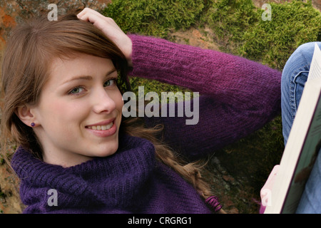 young woman leaning against a tree in a park and reading a book , Germany Stock Photo