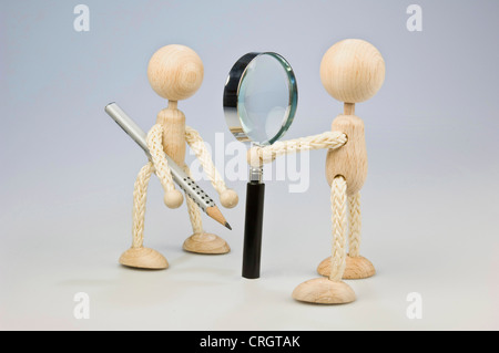 two wooden figures standing vis-a-vis, on with magnifier, one with pencil Stock Photo