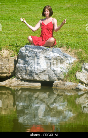 young woman practices yogaon a rock at a pond Stock Photo