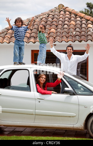 Family with two children waving to camera, boys standing on top of a car Stock Photo