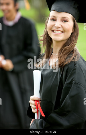 smiling female graduate standing outdoors with her diploma Stock Photo