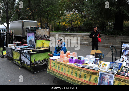Open-air market stall vendor sitting sidewalk tables selling paintings postcards soap candles, Union Square East, New York Stock Photo