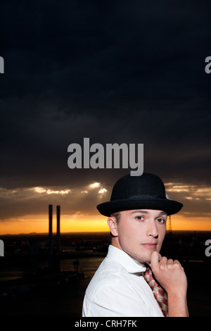 Portrait of confident young man wearing hat, posing in front of dark sky Stock Photo