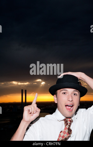 Portrait of young man wearing hat, pointing upward at dark sky Stock Photo