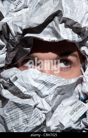 Curious young man looking through hole in crumpled newspaper Stock Photo