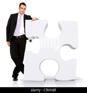 young business man leaning against a giant puzzle piece Stock Photo