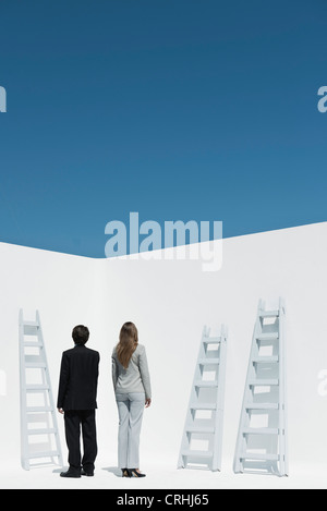 Professionals contemplating ladders, rear view Stock Photo