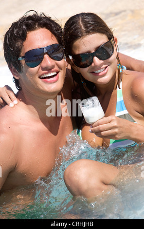 beautiful young couple in love having fun in a jacuzzi, wearing sunglasses and holding a cocktail Stock Photo