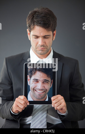 Man holding up digital tablet displaying image of himself smiling Stock Photo