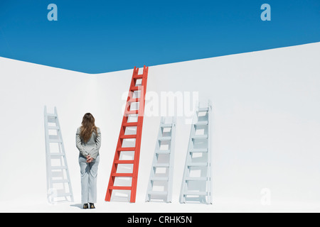 Businesswoman contemplating ladders, rear view Stock Photo