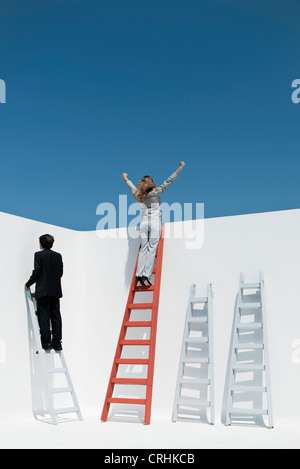 Businesswoman standing at top of ladder with arms raised in air Stock Photo