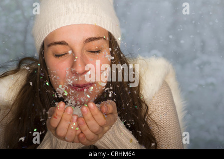 Young woman wearing winter clothing, blowing handful of confetti Stock Photo