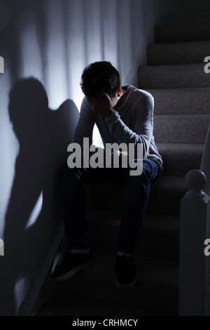 Young man sitting on the stairs, his hand covering his face. Stock Photo