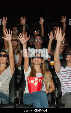 Audience wearing 3-D glasses in movie theater, arms reaching up Stock Photo