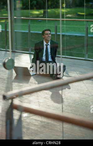 Businessman sitting on deck outdoors with laptop computer Stock Photo
