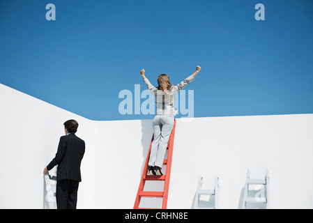 Businesswoman standing at top of ladder with arms raised in air Stock Photo