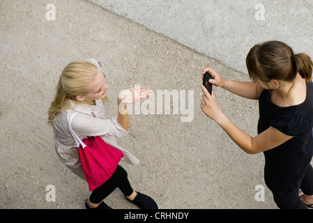 Young woman photographing friend with cell phone, elevated view Stock Photo