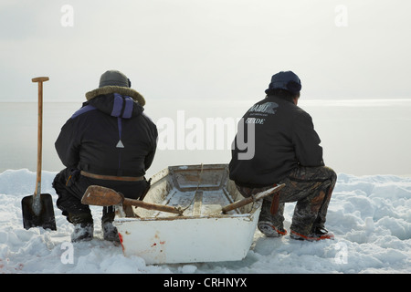 two Inuit sealers sitting at the ice edge on their rowing boat and look out on the open water, Greenland, Ostgroenland, Tunu, Kalaallit Nunaat, Scoresbysund, Kangertittivag, Kap Tobin, Ittoqqortoormiit Stock Photo
