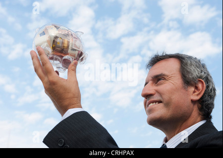 Mature man holding up transparent piggy bank filled with euros Stock Photo