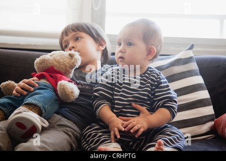 Boy sitting on sofa with arm around baby sister Stock Photo