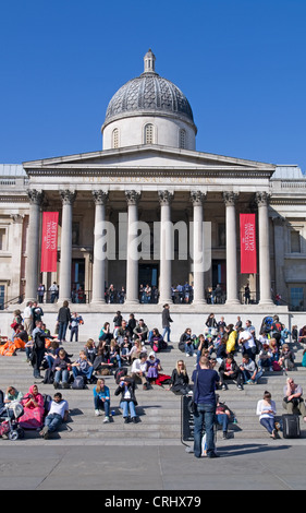 Tourists and sightseers on steps in Trafalgar Square in front of the main entrance of the National Gallery, London, England UK Stock Photo