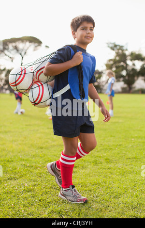 Boy carrying soccer balls on pitch Stock Photo