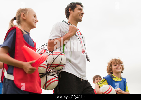 Coach carrying soccer balls on pitch Stock Photo