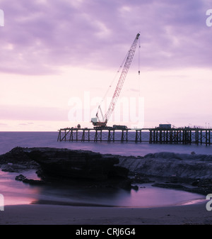 Sunset by the sea in the background is a crane on a pier to see Stock Photo