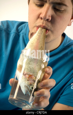 A young male pulls a fish from a glass of water using his teeth. Stock Photo