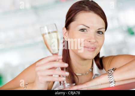 smiling young woman with long red brown hair and a glass of sparkling wine in hand Stock Photo