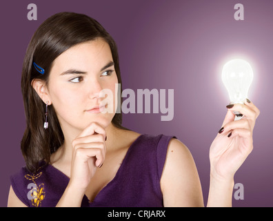 young woman thoughtfully looking at a glowing bulb in her hand Stock Photo