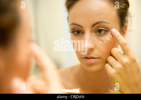 young woman putting on face cream in front of the mirror Stock Photo