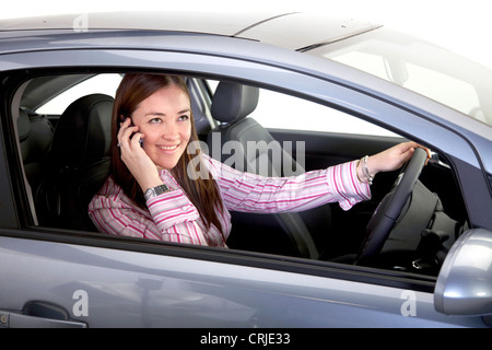 smiling young woman phoning with a mobile behind the steering wheel of a car Stock Photo