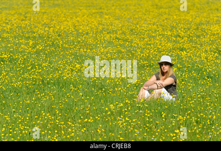 A girl sits in a meadow field of yellow buttercup flowers at Bampton, Cumbria Stock Photo