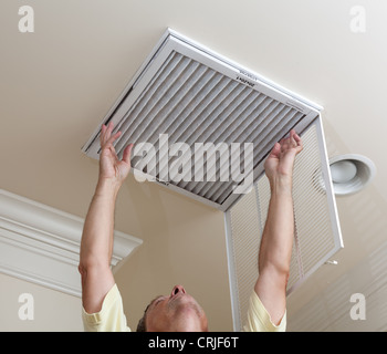 Senior male reaching up to open filter holder for air conditioning filter in ceiling Stock Photo