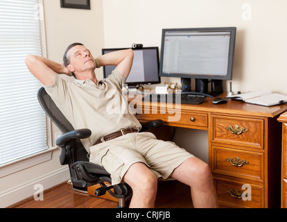 Man working from home office / thinking / slacking / sleeping / relaxing in shorts with desk with two monitors Stock Photo