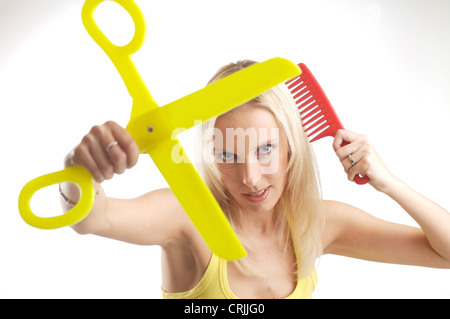 blond young woman with oversize comb and a pair of scissors Stock Photo
