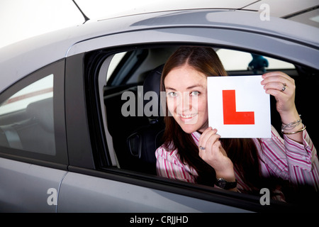 young woman sitting in a car holding up a sign with an 'L' (for 'learner'), United Kingdom Stock Photo