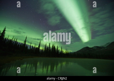 Aurora borealis fill the north sky over the Brooks Range and are reflected in a frozen tundra pond at 11:30pm Stock Photo